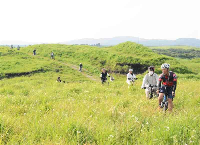 牧野ガイドの案内を受けながらマウンテンバイクで草原を走るツアーの参加者ら＝阿蘇市