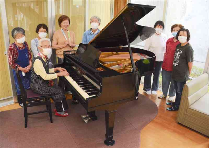 修復を終え、さかもと温泉センタークレオンに置かれたグランドピアノを囲む「夢俱楽部」のメンバーたち＝26日、八代市坂本町