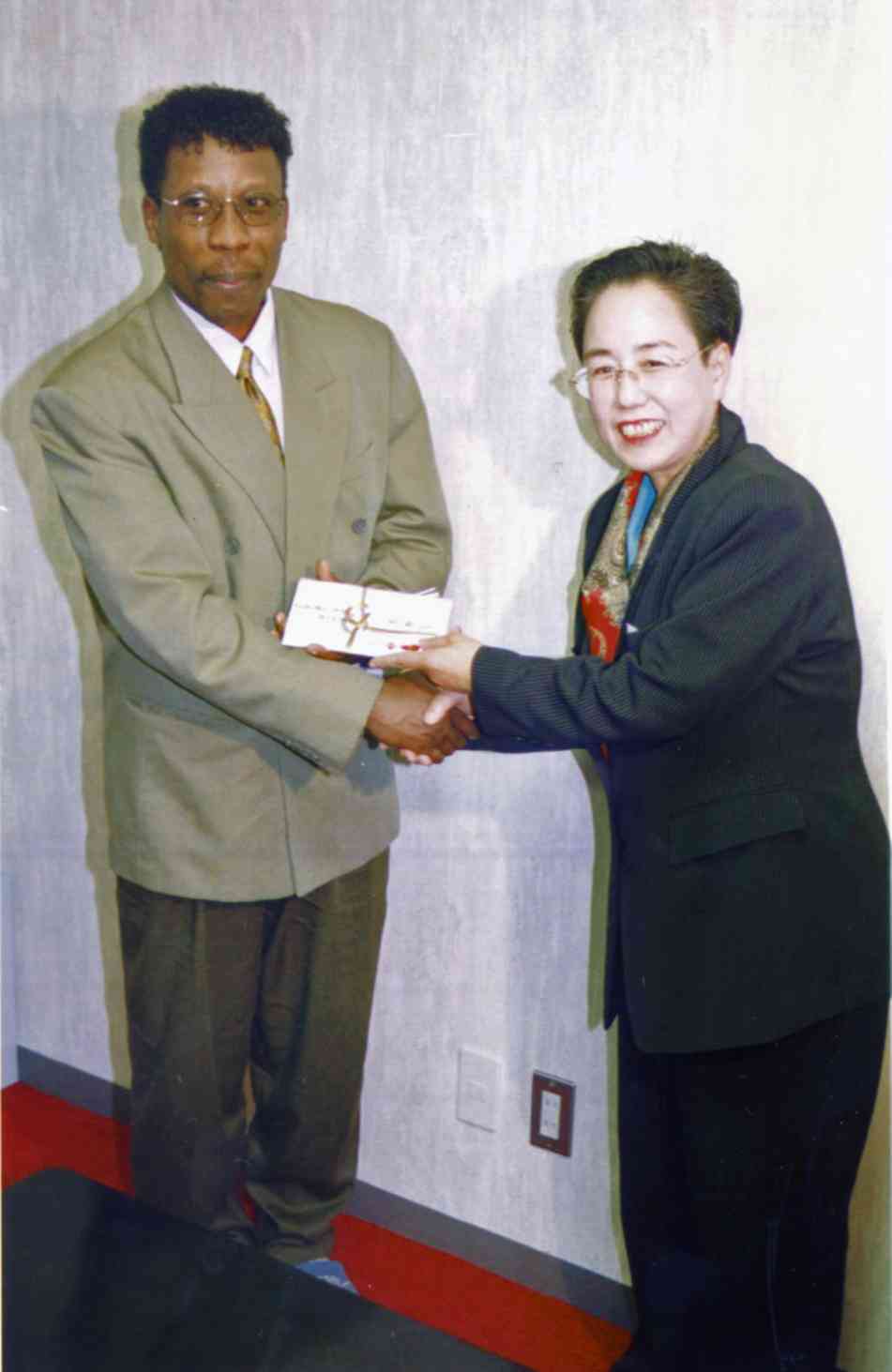 FAP患者を支援している「望みの会」の古賀清子会長（右）から研究支援金を贈られるマンブールさん＝1999年、荒尾市