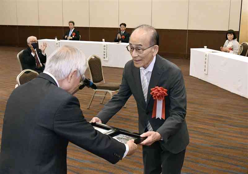 熊日賞を受賞し、河村邦比児熊日社長（左）から表彰されるジャーナリストの日下野良武さん。右奥は受賞者で染色家の高津明美さん＝4日午前、熊本市中央区のホテル日航熊本（大田垣典子）