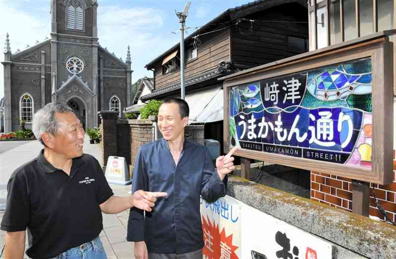 「﨑津うまかもん通り」の看板の前で談笑する財前俊也さん（左）と竹﨑吏さん＝天草市