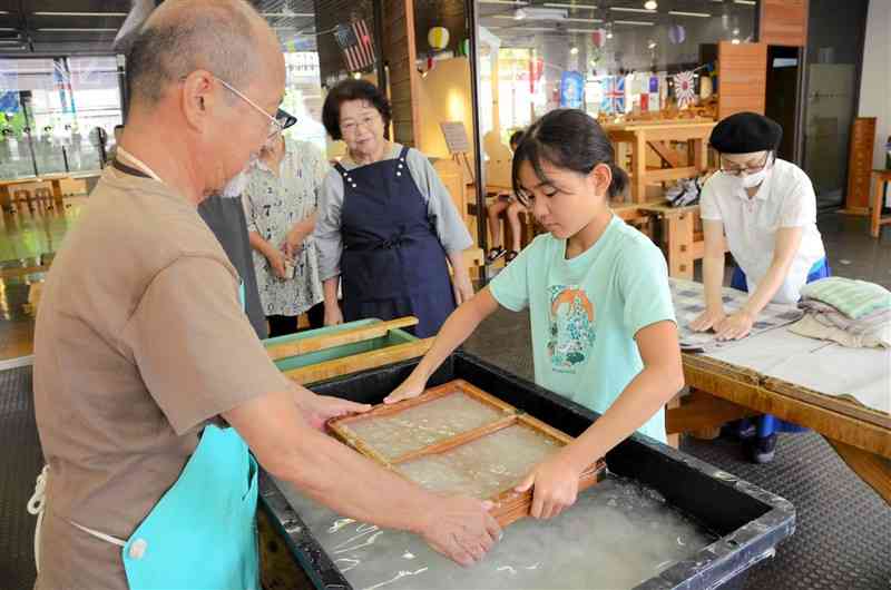 和紙職人の金刺潤平さん（左）から手すき和紙の手ほどきを受ける小学生ら＝熊本市中央区