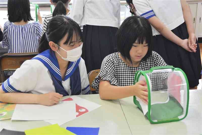 宇土高の生徒に教わりながら、色の違う紙を近づけて虫かごの中の蚊の反応を観察する児童＝宇土市