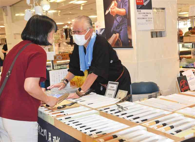 売り場で商品の説明を聞く買い物客＝16日、熊本市中央区