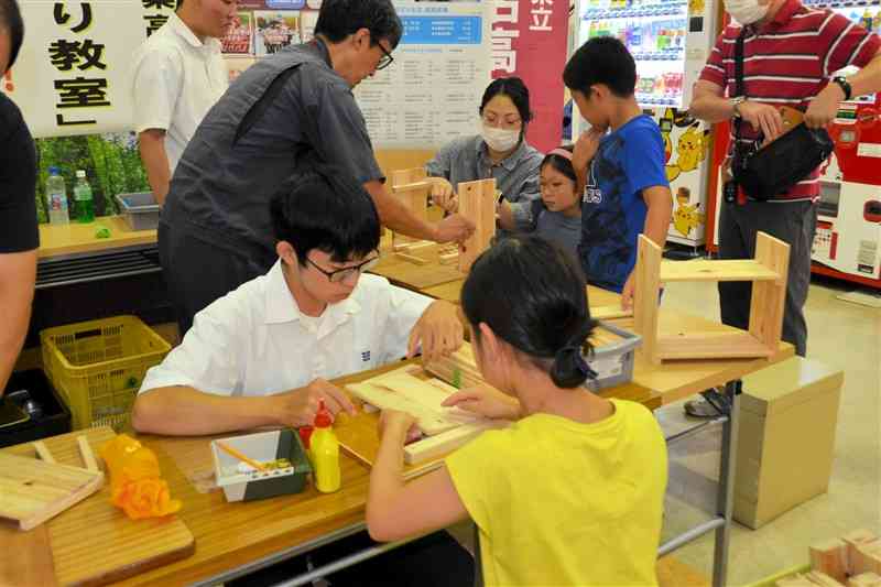 訪れた児童らに木製の調味料棚づくりを指導する玉名工高生ら＝玉名市