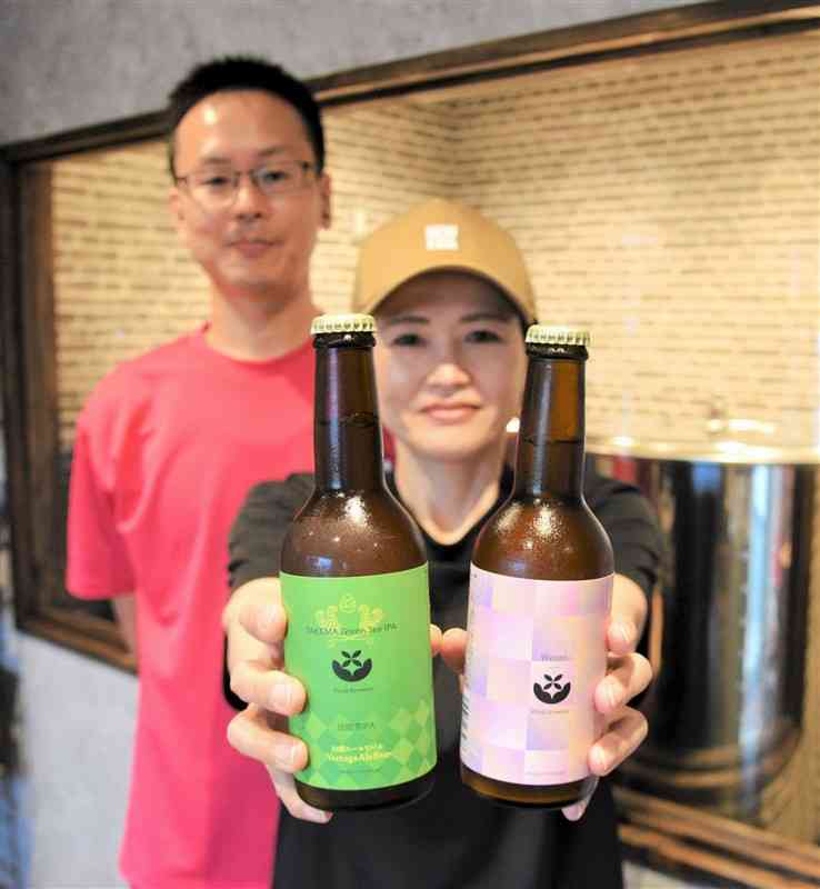 手作りのクラフトビールを手にしたキラリブルワリーの森ゆかりさん（手前）と、夫の淳二さん。後方はステンレス製の発酵釜＝山鹿市