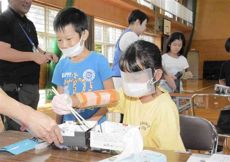 段ボールを腕に巻き、手袋をはめるなどして箸を使う児童＝熊本市東区