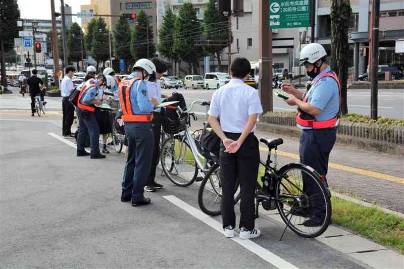 自転車の交通違反の一斉取り締まりで、イヤホン着用や並進などの違反者に指導警告する警察官＝25日、熊本市中央区