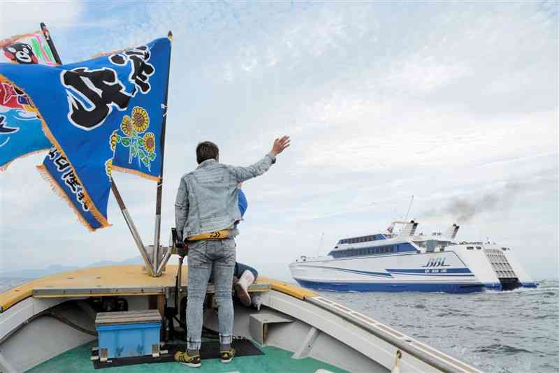 大漁旗を揚げた漁船から、修学旅行に出発する児童を見送る保護者＝熊本市西区