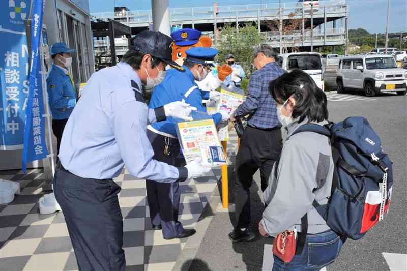 銀行の利用客に防犯グッズなどを手渡す県警備業協会のメンバーら＝13日、熊本市中央区