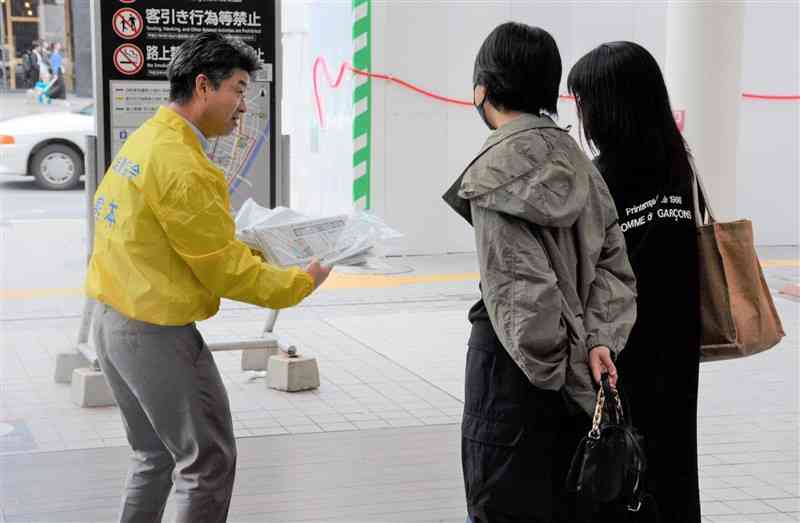 朝刊2紙が入った袋を手渡す県支部新聞公正取引協議会のメンバー（左）＝14日、熊本市中央区
