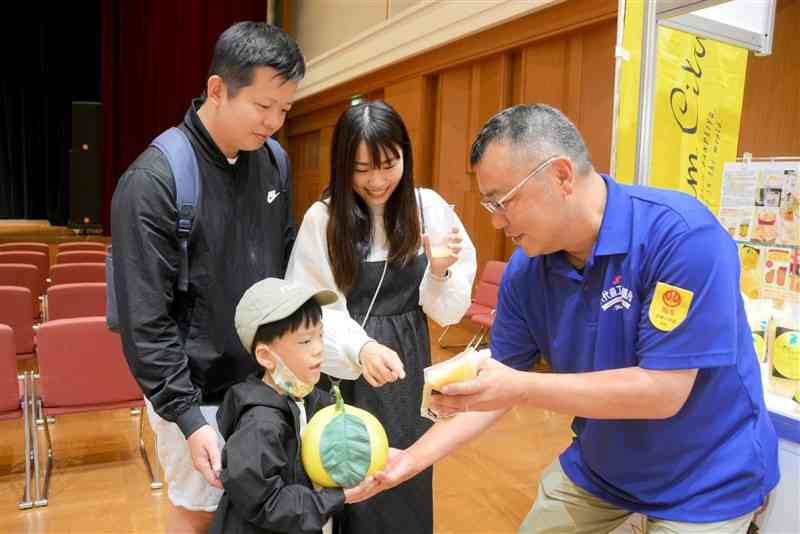 バンペイユの模型を持ち、ジュースを試飲する在熊台湾人の家族＝14日、熊本市中央区