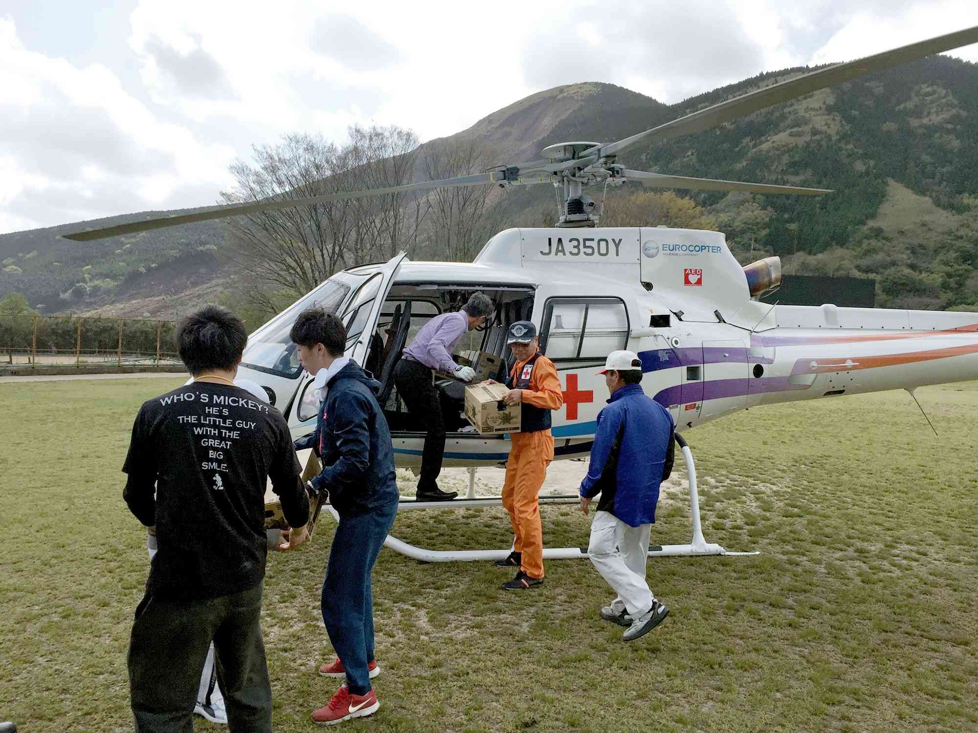 東海大阿蘇キャンパスに到着し、救援物資を下ろす赤十字飛行隊員。学生らが運搬を手伝った＝2016年4月17日