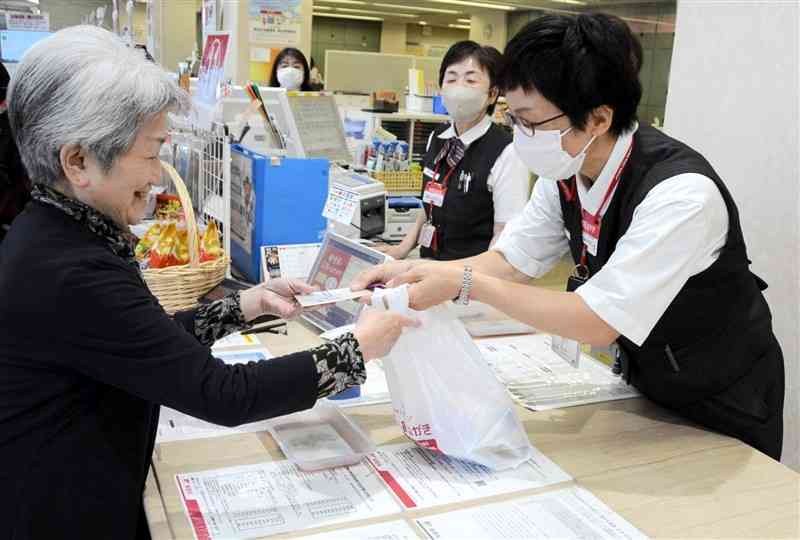 販売が始まった2024年用年賀はがきを受け取る購入者（左）＝1日、熊本市中央区