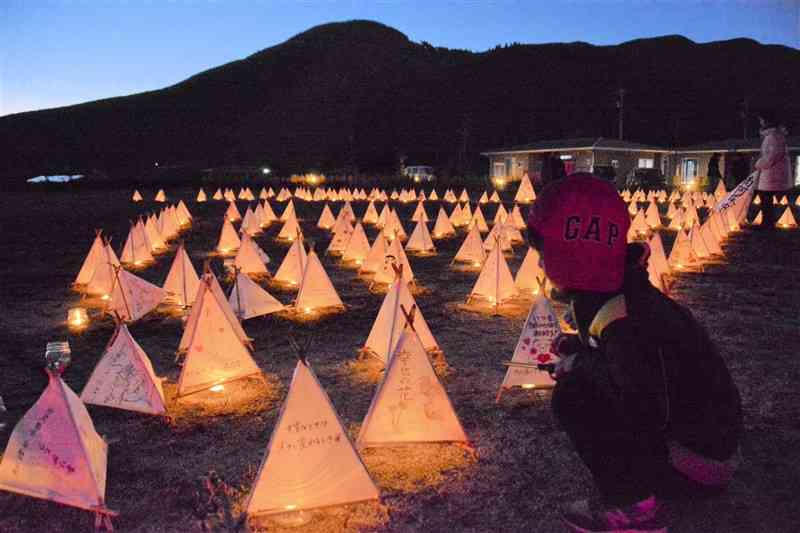 火がともされ、メッセージが浮かび上がった三角すいの紙灯籠＝12日、南阿蘇村