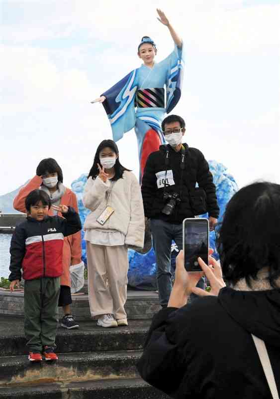 チェックポイントのハイヤ娘像の前で写真撮影する参加者たち＝18日、天草市