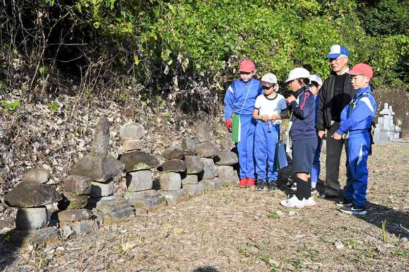 教良木城主一族のものとみられる五輪の塔群を見学する教良木小児童と永野隆一さん＝21日、上天草市