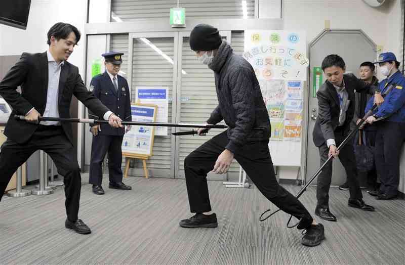 銀行強盗対応訓練で、刺股で強盗を取り押さえる熊本銀行の行員。1人が強盗の正面で対応し、もう1人が後方から足首を引っかけた＝28日、八代市