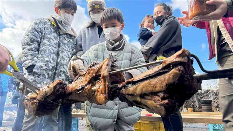 イノシシの丸焼きに、甲斐村長自慢のニンニクじょうゆをたっぷり塗り込む子ども