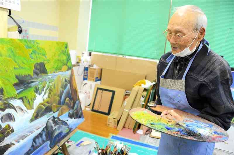 絵の具を乗せたパレットを片手に、「新緑の渓谷」について語る吉山安彦さん＝合志市
