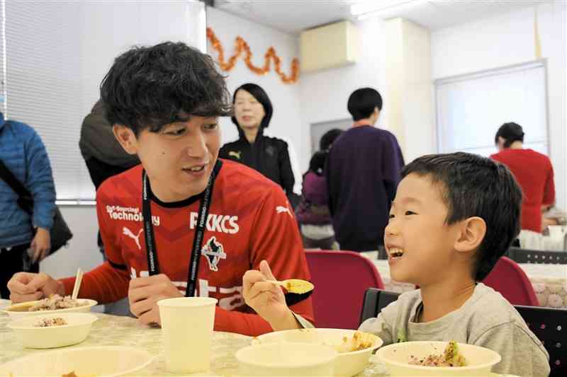 子どもたちと一緒にカレーライスを食べるロアッソ熊本の石川大地選手（左）＝2日、熊本市