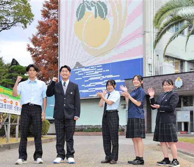 来年度からの新制服を一足先に着用する八代農業高の生徒。校舎の壁には、大きなバンペイユの絵が描かれている＝八代市