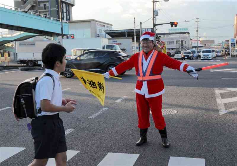 交通指導をする渡邉弘幸さん。小学校の2学期の終業式に合わせて、サンタクロースの格好で見守った＝22日、熊本市南区