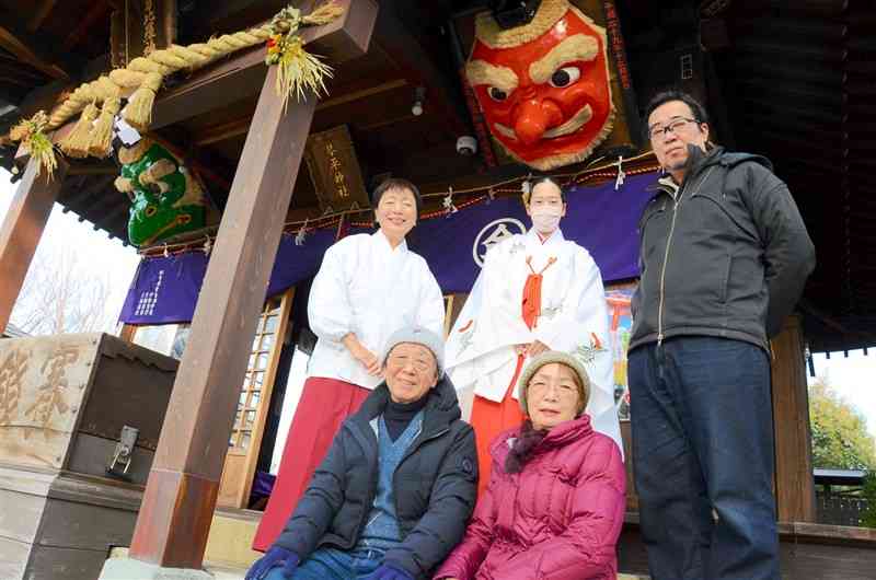 拝殿に飾られた赤い大天狗と緑のからす天狗のお面と修復した厚賀新八郎さん（手前左）ら＝26日、熊本市中央区