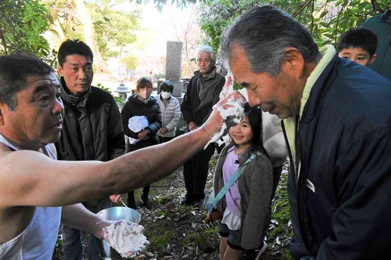 婿役の田中広徳さん（左）から、シトギを額につけてもらう地区の住民たち＝8日、菊池市