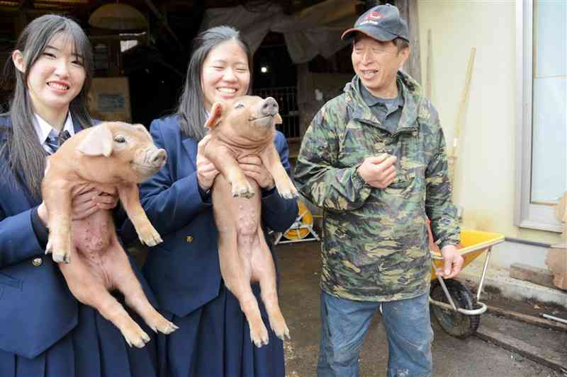 デュロック種の子豚を抱きかかえる熊本農高畜産科の生徒と、淋博道さん（右）＝21日、球磨村
