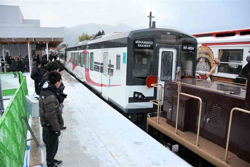 トロッコ列車の機関車でけん引されてきた南阿蘇鉄道の新車両に見入る人たち＝24日、高森町