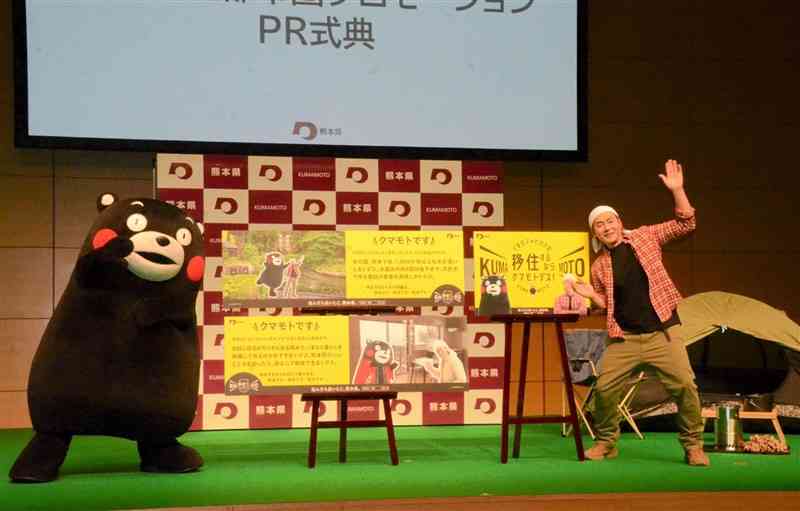熊本の魅力を紹介した広告パネルを紹介するお笑い芸人のヒロシさん。東京や大阪、福岡の電車内や駅に掲示される＝2日、東京都港区
