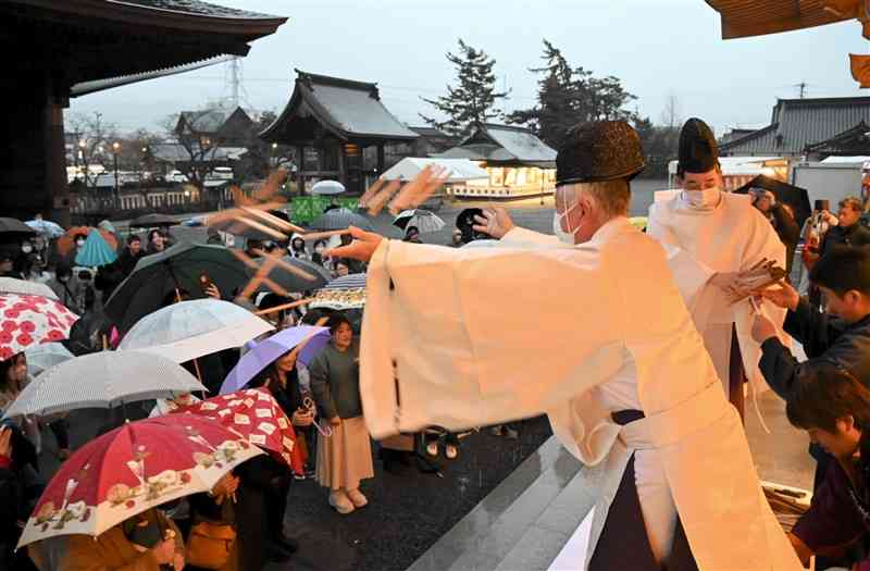 詰めかけた参拝者に護摩木をまく阿蘇神社の神職ら＝3日、阿蘇市