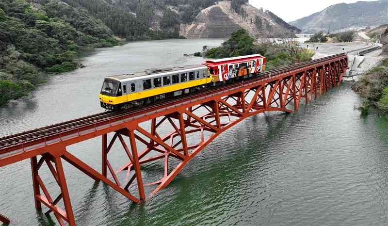 立野ダムの試験湛水で橋脚部分が水に沈んだ南阿蘇鉄道の第一白川橋梁。2両編成の臨時列車がゆっくりと通過した＝4日午前、南阿蘇村（ドローン撮影）