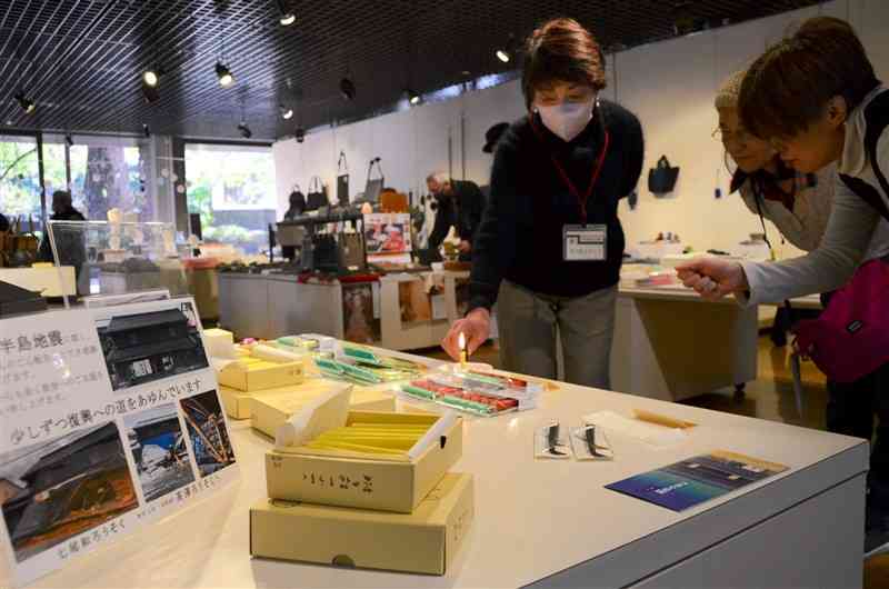 能登半島地震で被災した石川県七尾市産の和ろうそくが並んだ会場。損壊した店舗の写真（左）も展示している＝6日、県伝統工芸館