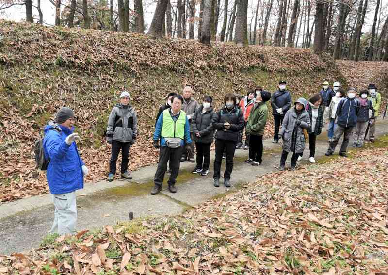 鞠智城のハイキングツアーで、土塁などの痕跡について学芸員（左端）の説明を聞く参加者たち＝3日、山鹿市菊鹿町