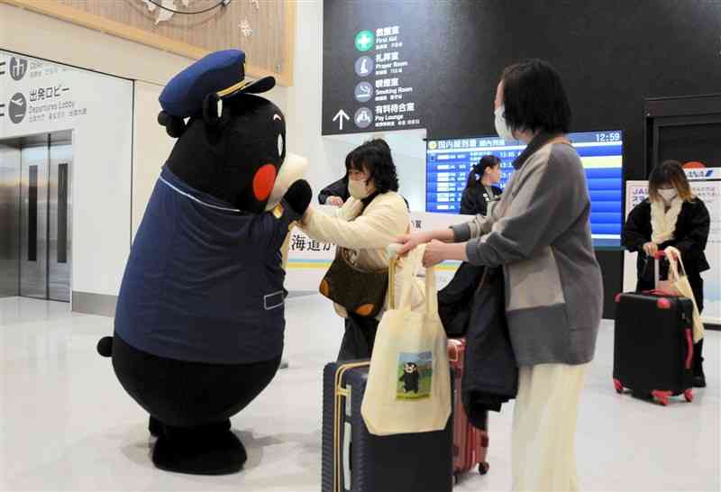 熊本空港の到着口で、くまモンの歓迎を受ける札幌からの旅行客ら＝8日、益城町
