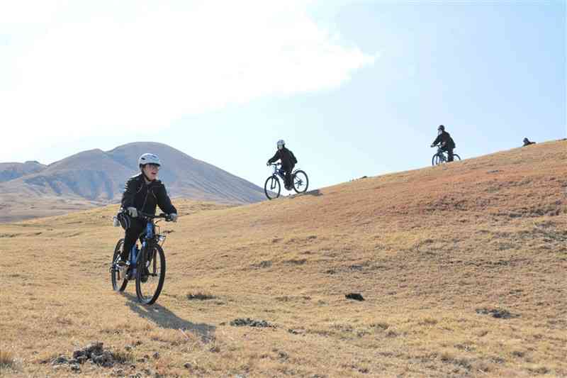 牧野を電動アシスト付き自転車で駆け抜ける阿蘇中央高の生徒ら＝16日、阿蘇市