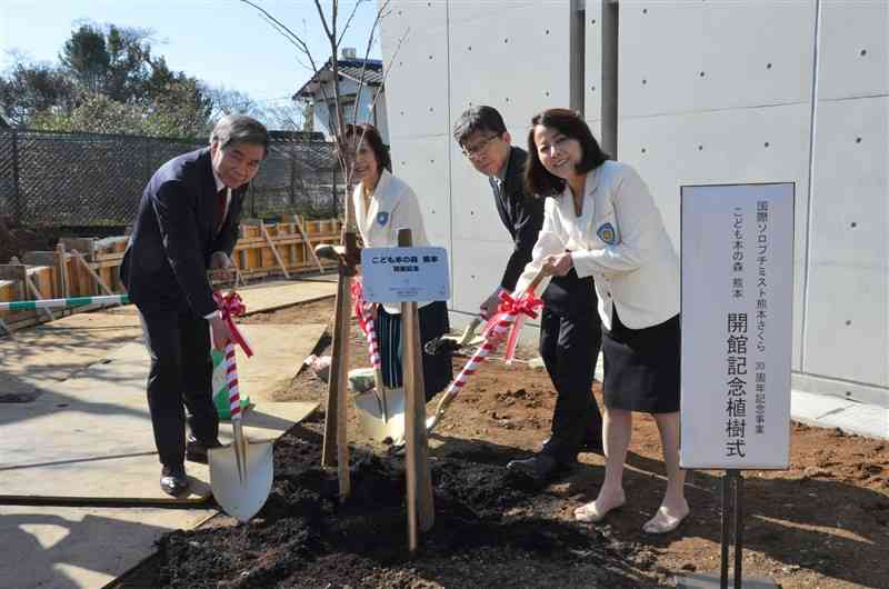 「こども本の森　熊本」の開館を祝い桜の木を植樹する、「国際ソロプチミスト熊本　さくら」の宮村裕子会長（右）と蒲島郁夫知事（左）ら＝17日、熊本市中央区