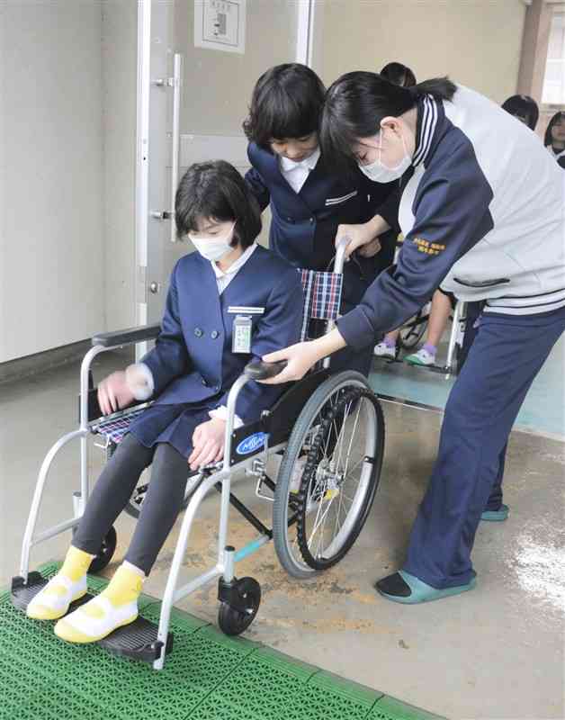 芦北高福祉科の生徒（右）からアドバイスを受けながら車いすを体験する水俣二小の児童ら＝21日、芦北町