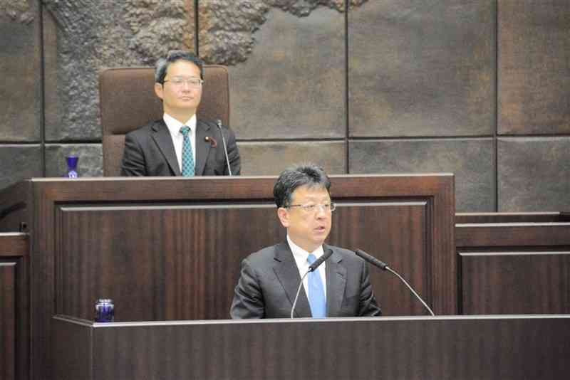 熊本市議会代表質問で、市役所本庁舎の建て替え場所を「今秋をめどに決める」と述べる大西一史市長（手前）＝28日、本会議場