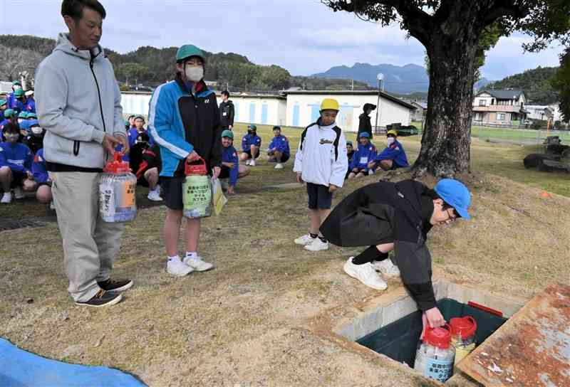 思い出の品などが入ったボトルをタイムカプセルの穴の中に置く菊鹿中の生徒＝7日、山鹿市