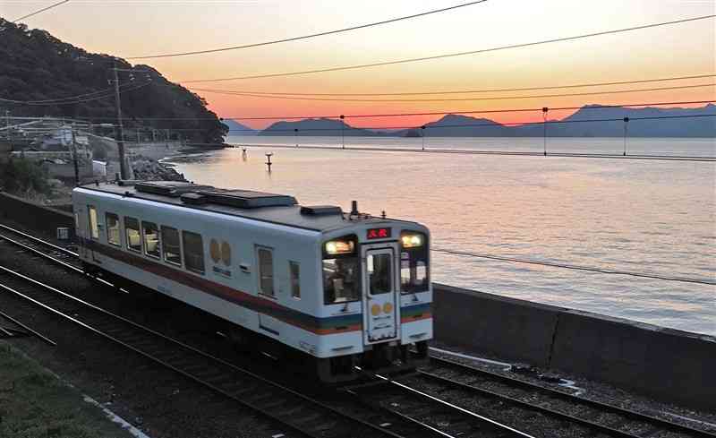 夕焼けを背に八代海沿いを走る肥薩おれんじ鉄道＝10日夕、芦北町（ドローン撮影、谷川剛）