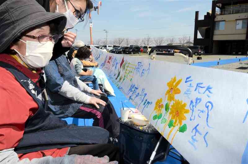 一枚の長い布に思い思いの絵を描く参加者ら＝16日、熊本市南区