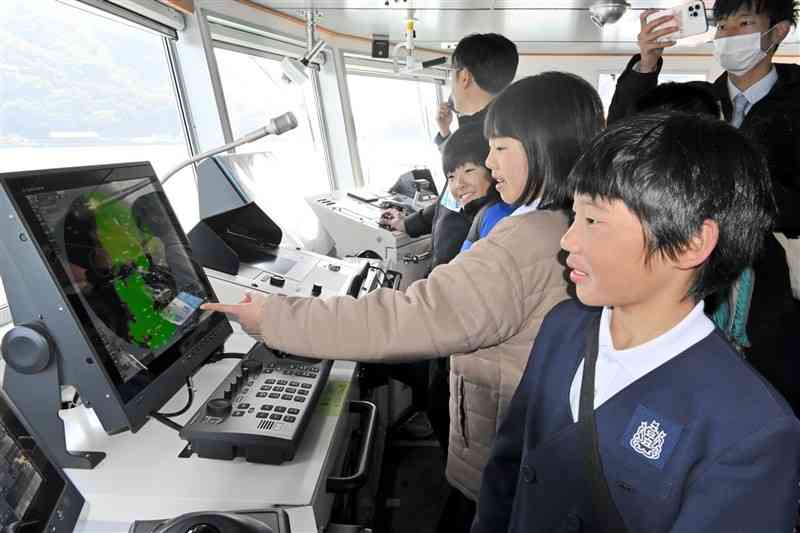 操舵室で、海図を映すモニターをのぞく登立小児童たち＝18日、宇城市