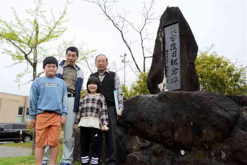 天草大水害の5年後に建てられた「災害復旧記念碑」。本田明男さん（後列右）は記念碑を紹介しながら、水害の記憶を伝えている＝7日、上天草市