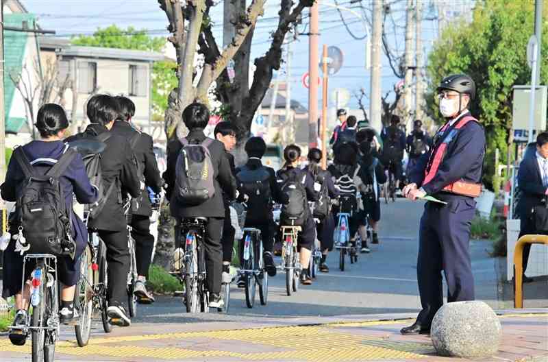 自転車用ヘルメットをかぶって交通指導に当たる八代署員＝10日、八代市