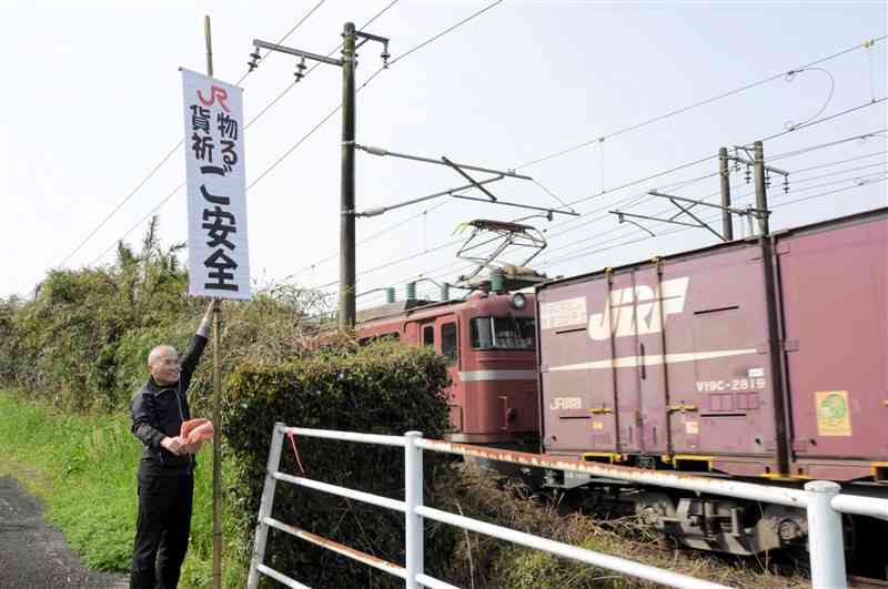JR貨物の貨物列車へ向けて「祈る　ご安全」と書かれた垂れ幕を掲げる石本今朝之さん＝16日午前9時頃、熊本市北区