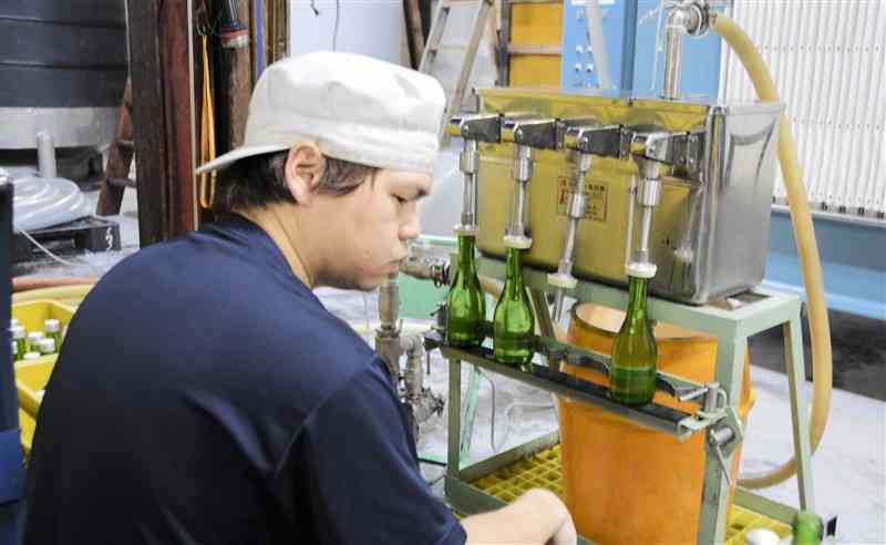 津奈木町産の酒米「山田錦」を使った新酒を瓶詰めする亀萬酒造の社員＝2月、同町
