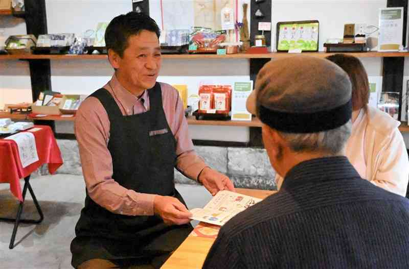 山鹿茶が味わえるカフェ店内で、山鹿の街のガイドをする木村元浩さん（左）＝4月22日、山鹿市